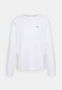 Weißes Langarm-Henley-Shirt aus strukturiertem Stoff mit Knopfleiste und einer linken Brusttasche mit kleinem Logo.
