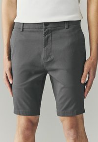 Grå shorts lavet af letvægtsmateriale, med knaplukning, bæltestropper og en skræddersyet pasform, der når lige over knæet.