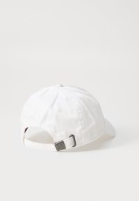 Hvid baseballkasket med en bøjelig skygge, justerbar rem bagpå og en metalaccent. Fremstillet af blødt, glat stof.