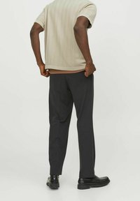 Beige texturerad stickad kortärmad skjorta, matchad med mörka skräddarsydda byxor och svarta skor, sedd bakifrån. Enkel, modern design.