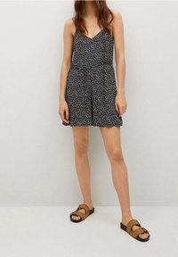 Romper con stampa floreale blu scuro, spalline sottili, vita cinchata e pantaloni shorts con vestibilità ampia. Abbinato a sandali scivolati marroni.