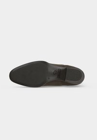 Chaussure marron à semelle en caoutchouc vue par le dessous montrant l’avant-pied et le talon texturés pour une meilleure adhérence, taille 37 indiquée, et logo de la marque près de la voûte plantaire.