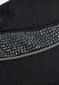 Čierna látka so pásom malých, tesne usadených čírych kamenčekov a reflexným strieborným prúžkom pod nimi.