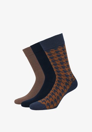 Trzy pary skarpetek w różnych odcieniach: brązowym, granatowym oraz brązowo-granatowym wzorze. Żebrowane wierzchy, gładkie tekstury i średnia wysokość.