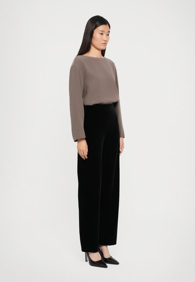 Haut marron à manches longues avec un décolleté carré, associé à un pantalon en velours noir à jambes larges et des escarpins noirs à bout pointu.
