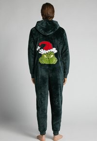 Ciemnozielony, pluszowy kombinezon z kapturem, z dużą haftowaną twarzą Grincha i czapką Mikołaja na plecach. Elastyczne ściągacze przy nadgarstkach i kostkach.