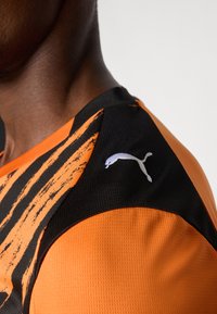 Orange og sort atletisk trøje med en tekstureret overflade, dristige striber og et hvidt Puma-logo på skulderen.