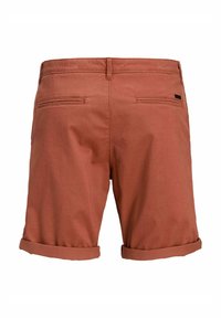 Rust-colored shorts made of woven fabric, featuring two back pockets and rolled cuffs. Minimalistic design with subtle branding detail.