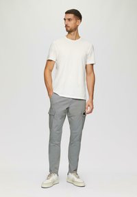 Witte T-shirt met korte mouwen, gecombineerd met lichtgrijze cargobroek met zijzakken en een zwarte sluiting, aangevuld met witte sneakers.