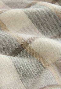 Wollendecke mit einem klassischen Karomuster in Beige, Creme und Hellgrau, mit einer weichen, strukturierten Oberfläche und warmem Aussehen.