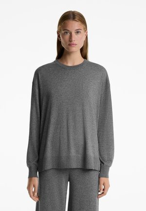 Maglione grigio a maglia con maniche lunghe, colletto rotondo e vestibilità rilassata. Il tessuto appare morbido, con una fine texture e orlo a coste.