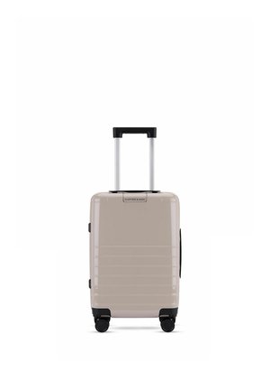 Valise cabine rigide beige avec poignée télescopique, quatre roues noires pivotantes et design rainuré horizontal.