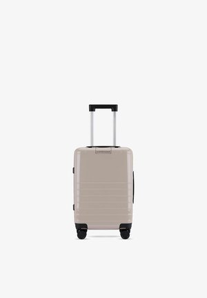 Valise cabine rigide beige avec poignée télescopique, quatre roues noires pivotantes et design rainuré horizontal.