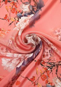 Tela de seda coral con un estampado floral, que presenta flores rosas y moradas, hojas naranjas y una textura suave, dispuestas en un patrón en espiral.