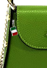 Groene neplederen handtas met gouden kettingaccenten, voorzien van neon groene stitching en een klein vlagvormig hangertje in rood, wit en groen.