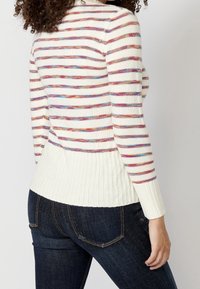 Pull rayé crème avec des rayures multicolores. Caractéristiques : ourlet et poignets côtelés, texture tricot légère, et silhouette ajustée.
