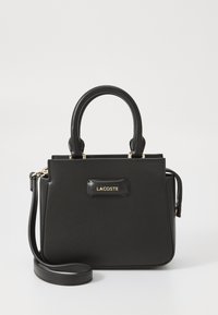 Sac à main Lacoste noir avec un design structuré, texture lisse, poignées supérieures et une bandoulière amovible. Présente un accent de logo doré.