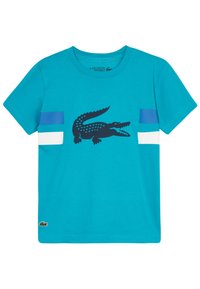 Turkusowa bawełniana koszulka z czarnym nadrukiem krokodyla oraz niebiesko-białymi poziomymi paskami na rękawach. Okrągły dekolt, krótkie rękawy.