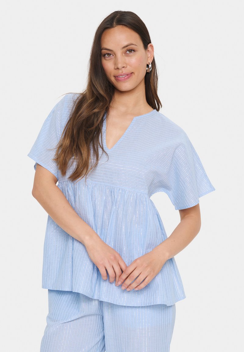Light blue relaxed-fit top with V-neck, short sleeves, and pleated detail. The fabric features subtle vertical stripes and a smooth texture.