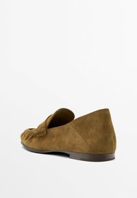 Brązowy zamszowy mokasyn z niskim obcasem, przeszyciami w stylu mokasyna i zaokrąglonym noskiem, widziany z tylnego boku.