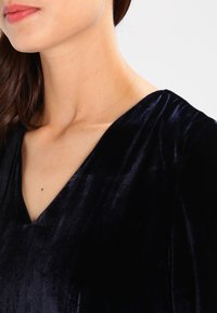 Top de terciopelo Marino con un profundo escote en V, textura suave y suave brillo, que destaca el rico color y la elegante caída de la tela.