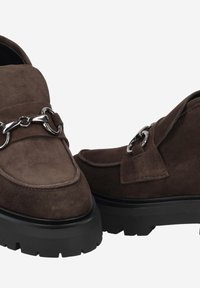 Brown suede loafers with a chunky black sole, featuring silver chain hardware and a smooth rounded toe. Textured material with accent details.