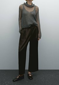 Pull gris tricoté avec col châle, associé à un pantalon large noir. Chaussures noires à enfiler avec un accent rond argenté. Couleur unie et tissu texturé.