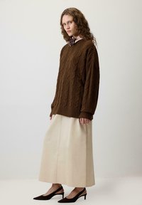 Brown cable knit sweater with oversized sleeves, paired with a long cream skirt and black slingback heels. Textured yarn detail is visible.