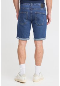 Kratke jeans hlače, temno modre, dolžine do sredine stegen z zavihanimi robovi. Dva zadnja žepa, ravno prileganje in črna usnjena etiketa na pasu.