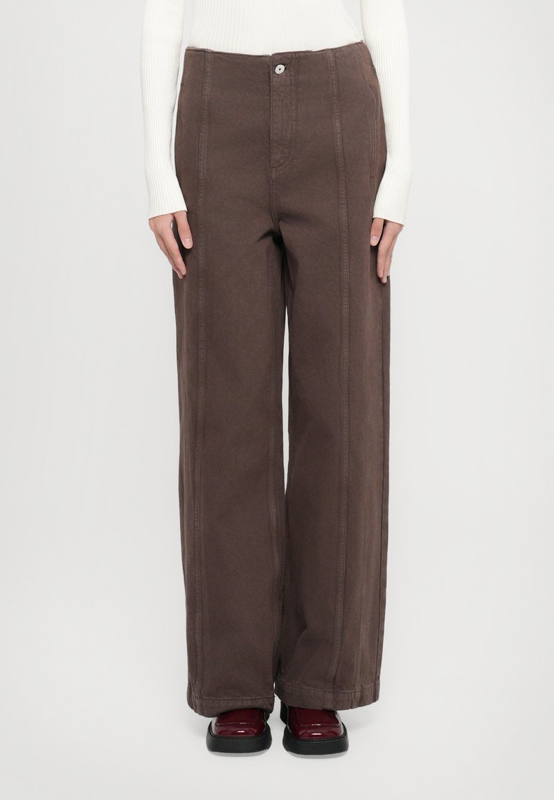 Brown wide-leg pants made of durable fabric, featuring visible stitching and a front button closure. Paired with dark red footwear.