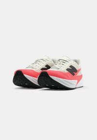 Sport Schuhe mit einem cremefarbenen Obermaterial, schwarzen Akzenten und einer leuchtend rosa Sohle. Verfügt über ein strukturiertes, schwarzes Gummi-Profil für guten Halt.