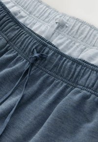 Deux pantalons de survêtement à taille élastique, l'un gris clair et l'autre gris foncé, tous deux munis de cordons de serrage noués.