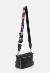 Sac bandoulière en cuir noir avec une sangle florale, fermeture éclair, accents latéraux à carreaux et sangle réglable pour un port polyvalent.
