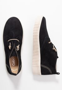 Černé semišové boty s vysokým svrškem, krémovou gumovou podrážkou, elastickými tkaničkami a kontrastním béžovým prošíváním.