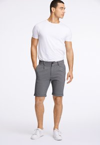 Graue Shorts aus strukturiertem Stoff, mit umgeschlagenen Säumen, seitlichen Taschen und Knopfverschluss, kombiniert mit einem schlichten weißen T-Shirt.