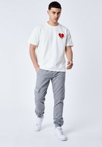 Camiseta de algodón blanca con un gráfico de corazón rojo, combinada con pantalones cargo grises con bolsillos laterales y zapatillas blancas.