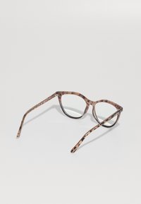 Gafas de sol de forma de gato en carey marrón con lentes transparentes y esquinas puntiagudas. El acento en la patilla presenta la marca "Quay."