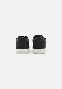 Black sneakers with a smooth leather upper, rounded toe, and white rubber sole. Features minimal stitching and a minimalist design.