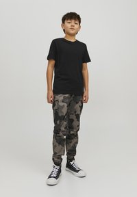 T-shirt nera in cotone abbinata a pantaloni cargo mimetici grigi e neri, dotati di tasche e polsini elastici, indossata con sneaker alte nere.