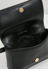 Wnętrze czarnej skórzanej torebki na ramię z zapięciem na zatrzask, z złotym akcentem i nazwą marki "MICHAEL KORS" wytłoczoną na złoto.