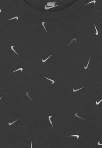 Czarna koszulka z rozproszonym wzorem białych i szarych logo Nike na teksturowanej tkaninie. Okrągły dekolt, casualowy krój.