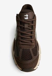 Brauner Sneaker aus Mesh- und Wildledermaterialien mit Schnürdesign, strukturierten Überzügen und einer kontrastierenden sandfarbenen Sohle. Silbernes Logo an der Seite.