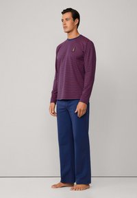 Camisa de manga larga a rayas en azul oscuro y burdeos, combinada con pantalones navy lisos. La camisa presenta un pequeño emblema en el pecho.
