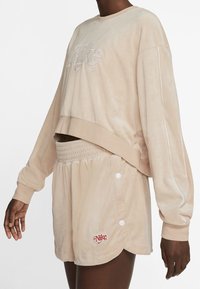 Beige velour kortad sweatshirt med vit broderi och matchande högmidjade shorts med knapppart och röd logodetalj.