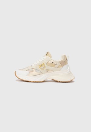 Sneaker chunky beige e bianco con pannelli in rete e pelle, lacci bianchi, suola in gomma e un logo giallo stilizzato sul lato.