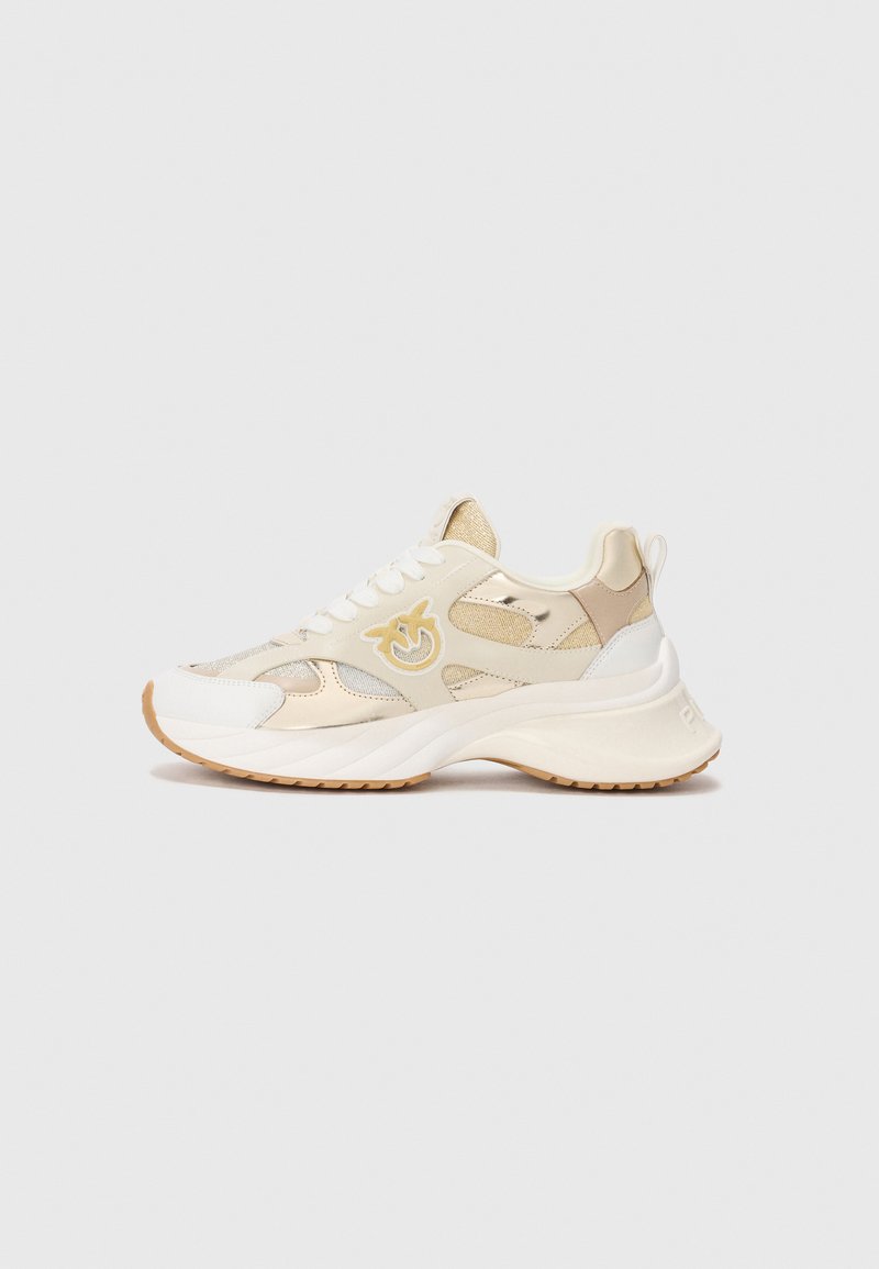 Beige og hvite chunky sneakers med mesh- og lærpaneler, hvite snøringer, gummisåle, og en stilisert gul logo på siden.