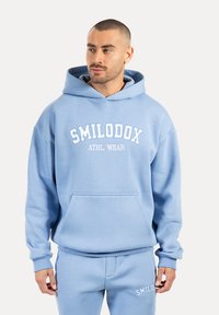 Sudadera con capucha de color azul claro, con bolsillo frontal, logo "SMILODOX ATHL. WEAR" en blanco, hecha de tela suave con puños y dobladillo acanalados.