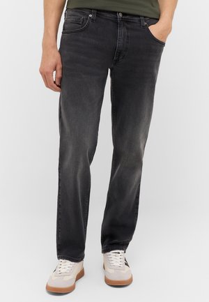 Dunkelgraue Jeans aus Denim mit geradem Bein, fünf Taschen und einer subtilen verblichenen Textur. Kombiniert mit hellen Sneakers.