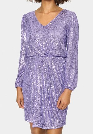 Kvinde iført en langærmet, lilla palietkjole med V-udskæring og samlet talje, stående foran en ensfarvet baggrund.