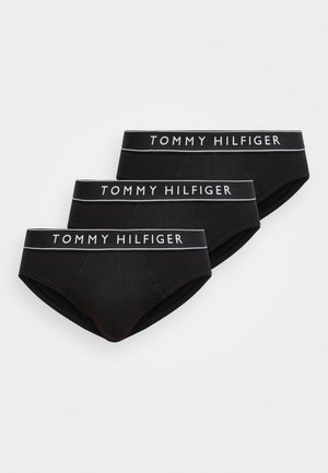 Drei schwarze Tommy Hilfiger Slips übereinandergelegt, jeder mit weißem Logo-Schriftzug auf den elastischen Bundbändern vor einem einfachen weißen Hintergrund.